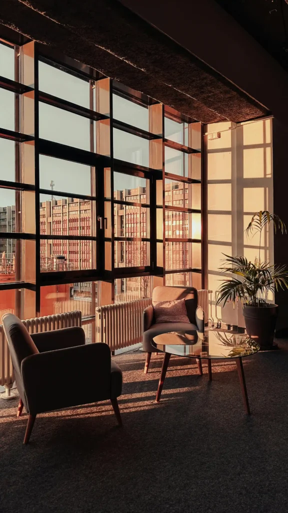Elegancka strefa wypoczynkowa po remoncie – przeszklona ściana, fotele mid-century i żeliwne grzejniki w nowoczesnym wnętrzu